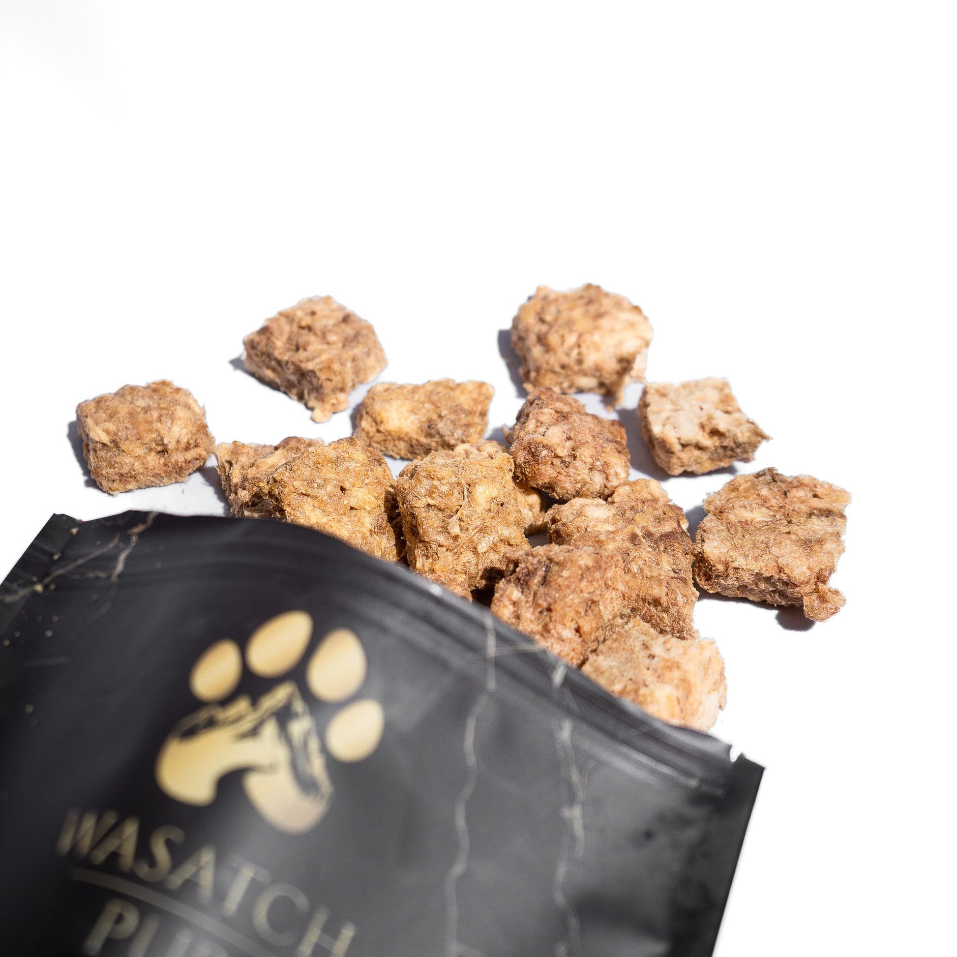 Wasatch Pup natural single-ingredient freeze-dried chicken crisps dog treats spilling from the bag.