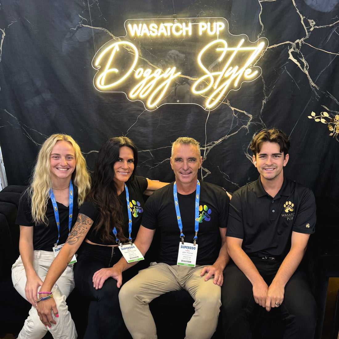 Four people posing together in front of a 'Wasatch Pup Doggy Style' sign.